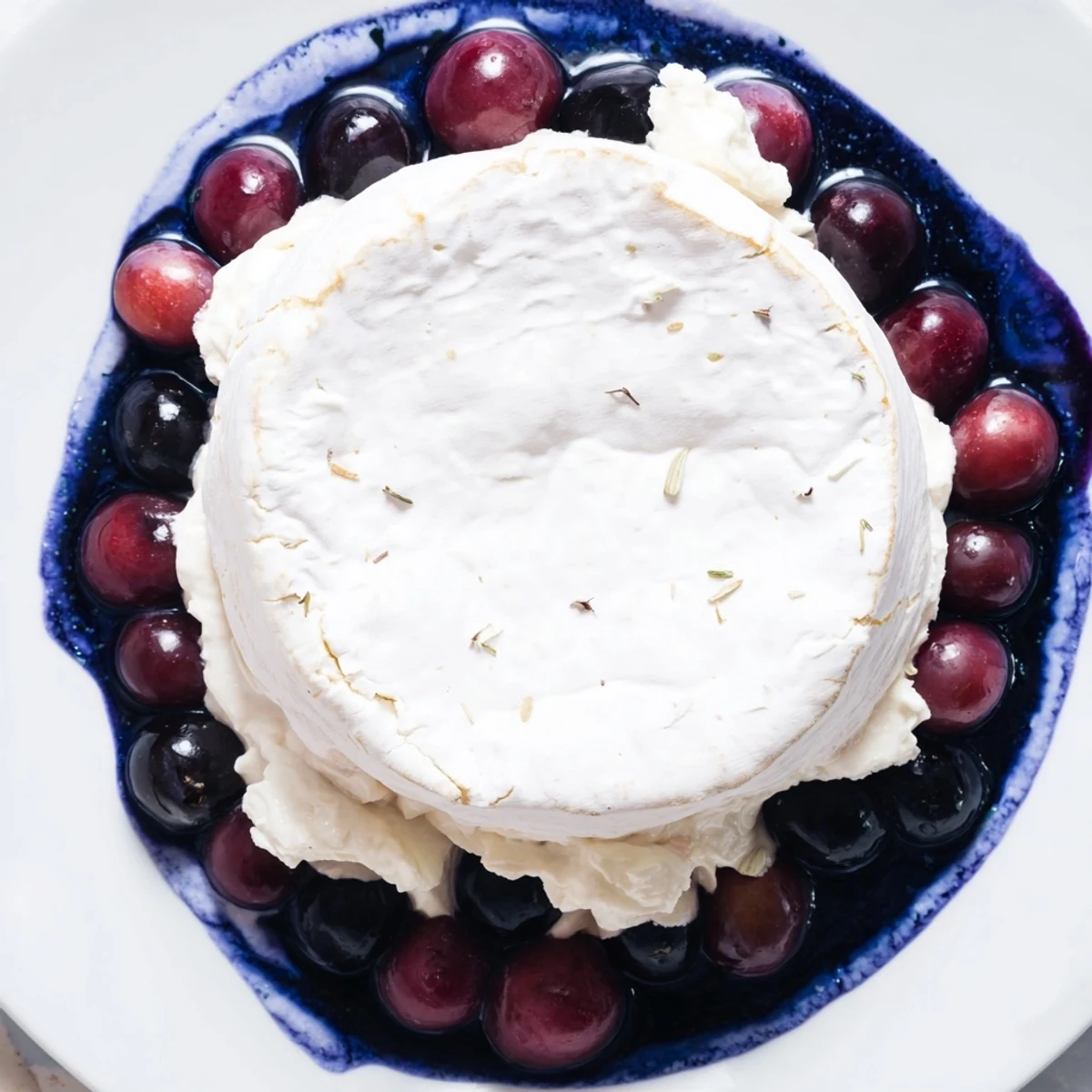 This "Floating Island" appetizer presents a whole cheese wheel on blue yogurt with dark grapes as a vibrant garnish.
