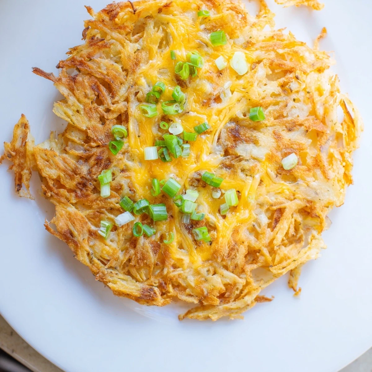 A stack of savory Cheesy Hash Brown Waffles with melted cheese and fresh green onion garnish.