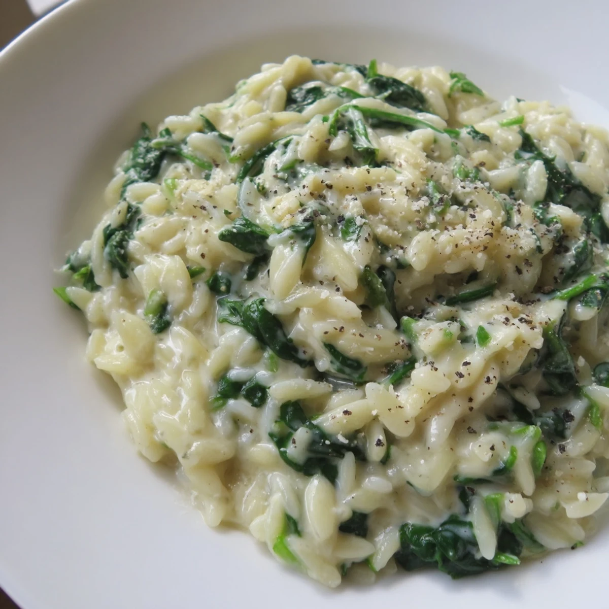 Creamy Spinach Orzo, a comforting one-pan meal, bubbling in a skillet with melting Parmesan cheese.