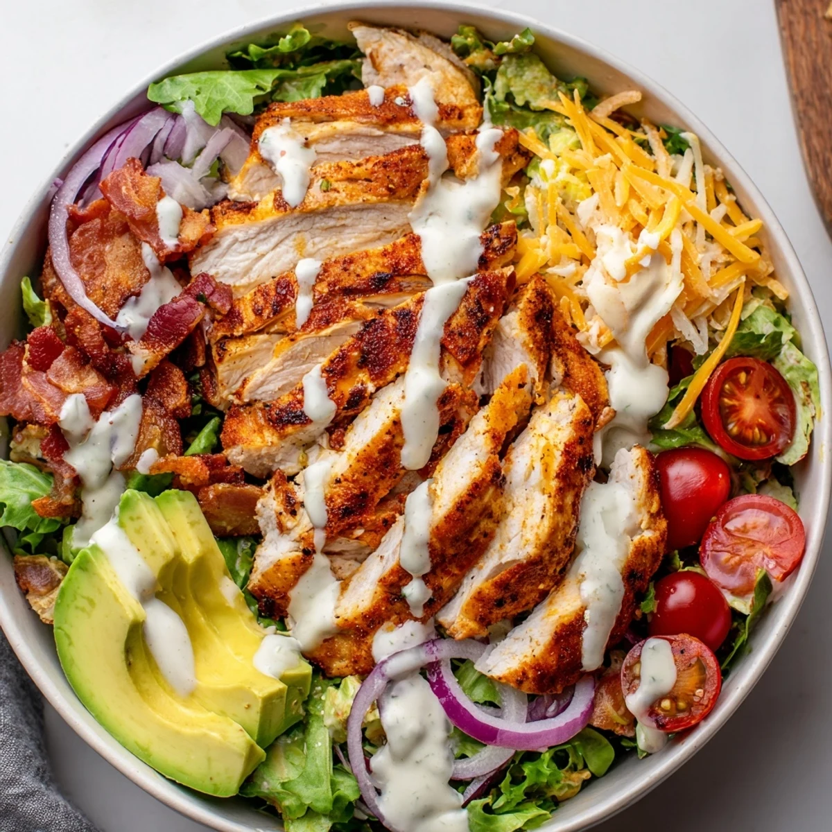Sliced chicken and crispy bacon atop a colorful, fresh crispy bacon chicken salad, ready to eat.