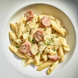 A close-up shot of Smoked Sausage Cajun Alfredo with parsley garnish and grated Parmesan.