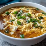 Delicate Chinese-style egg drop soup featuring aromatic broth and wispy egg swirls in a warm bowl.  