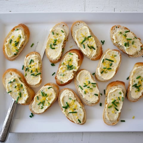 A close-up of golden Vodka Butter Crostini spread with creamy vodka butter, garnished with fresh chives and lemon zest.