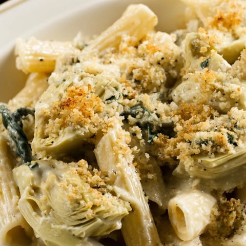 Golden-brown Artichoke Pasta Bake bubbling from the oven, featuring creamy Parmesan sauce, tender pasta, fresh spinach, and marinated artichoke hearts.