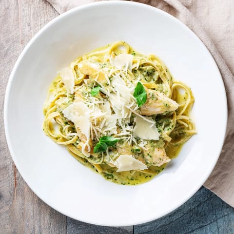 Creamy pesto egg and chicken pasta topped with fresh Parmesan and vibrant basil garnish.