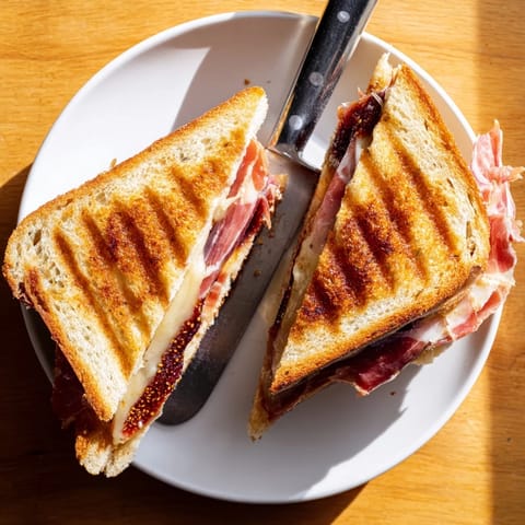 Close-up of a Crispy Prosciutto & Fig Panini, showcasing salty prosciutto and sweet fig jam between crisp Italian bread.  