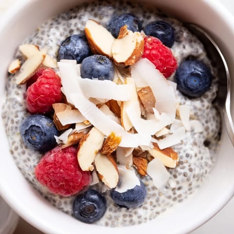 Stirred Poppy Seed Chia Pudding reveals a creamy texture speckled with black poppy seeds, served in a rustic bowl alongside sliced almonds and maple syrup.
