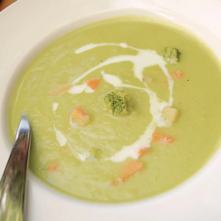 A spoon dipping into a bowl of Creamy Broccoli Soup next to toasted artisan bread