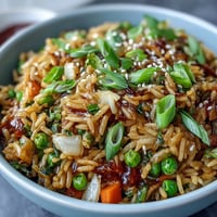 Close-up of orzo fried rice with vibrant peas and carrots, deliciously savory.